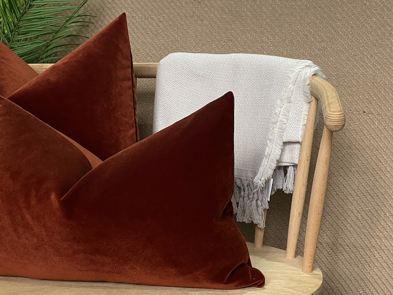 Peut inclure: Deux coussins de canap&eacute; en velours rouille sur une chaise en bois avec une couverture blanche jet&eacute;e sur le dossier.