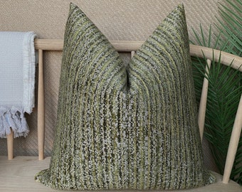 May include: A green and white patterned throw pillow with a textured fabric. The pillow is sitting on a wooden bench.