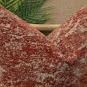 Op de afbeelding: Een roestkleurig kussen met een wit en roestkleurig geometrisch patroon. Het kussen is gemaakt van een zachte, textuurrijke stof.