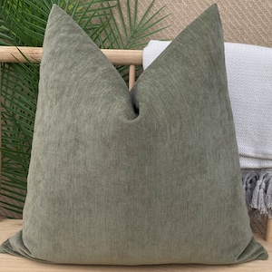 May include: A green square throw pillow with a textured fabric. The pillow is sitting on a wooden bench.