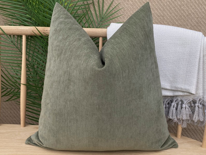 May include: A green square throw pillow with a textured fabric. The pillow is sitting on a wooden bench.