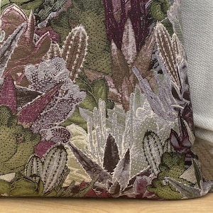 May include: Close-up of a decorative pillow with a floral pattern featuring purple, green, and white flowers. The fabric has a textured, woven look.