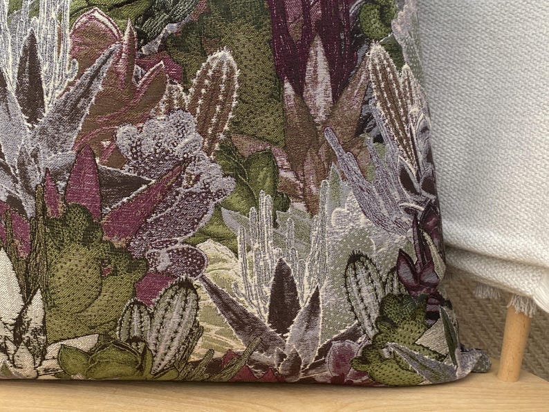 May include: Close-up of a decorative pillow with a floral pattern featuring purple, green, and white flowers. The fabric has a textured, woven look.