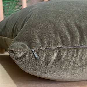 May include: A close-up of a dark green velvet cushion with a zipper closure. The cushion is soft and plush, and the zipper is hidden.