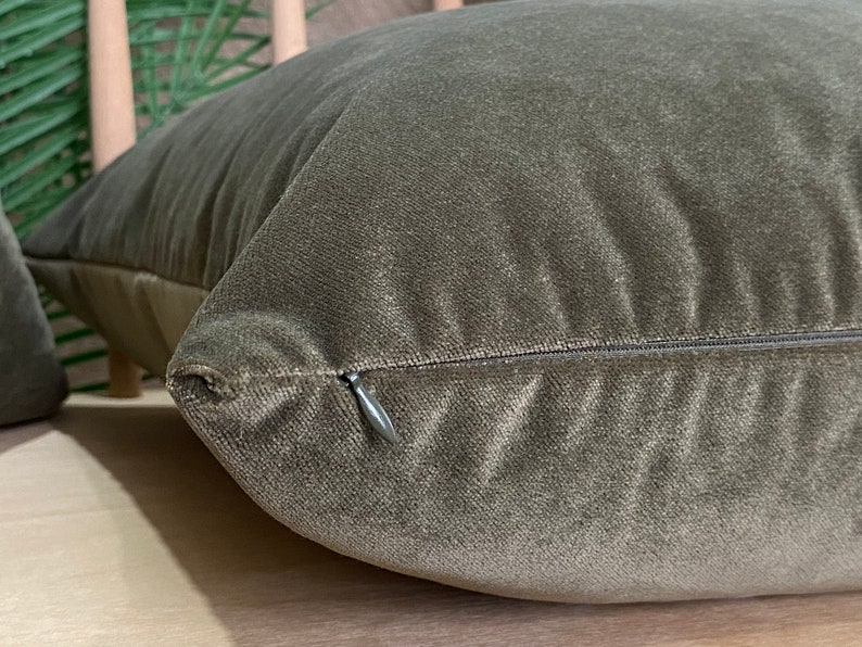 May include: A close-up of a dark green velvet cushion with a zipper closure. The cushion is soft and plush, and the zipper is hidden.