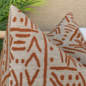 May include: Two throw pillows featuring a geometric pattern in shades of brown and beige. The pillows are made from a textured fabric with a subtle sheen.