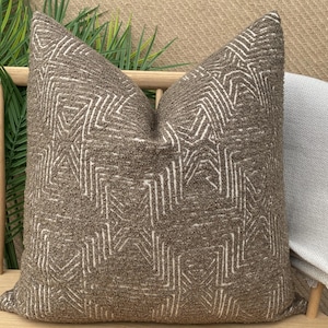 Könnte beinhalten: Ein braunes Kissen mit einem weißen geometrischen Muster. Das Kissen ist aus einem weichen, strukturierten Stoff.