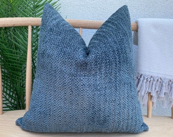 May include: A blue textured throw pillow with a square shape. The pillow is sitting on a wooden bench.