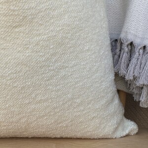 May include: A white throw pillow with a textured surface. The pillow is made of a soft, woven fabric.