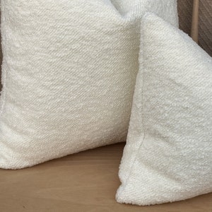 May include: Two white throw pillows with a textured surface. The pillows are made of a soft, fluffy material.
