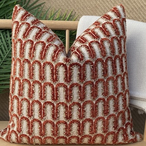 Puede incluir: Una almohada decorativa con un patrón geométrico en tonos naranja y blanco. La almohada está hecha de una tela suave y texturizada.