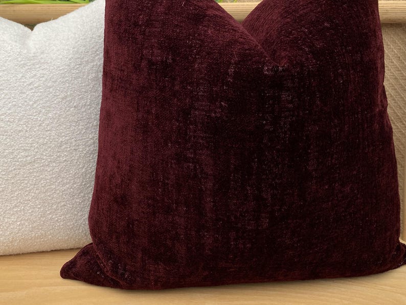 Pu&ograve; includere: Due cuscini decorativi. Uno &egrave; di colore bordeaux scuro con un aspetto strutturato e vellutato. L'altro cuscino &egrave; bianco con una superficie strutturata e nodosa. I cuscini sono probabilmente per l'arredamento della casa.