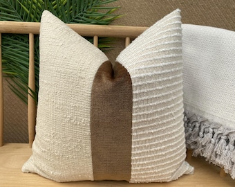 Puede incluir: Una almohada de tiro blanca y marrón con una tela texturizada. La almohada tiene una franja marrón en el centro.