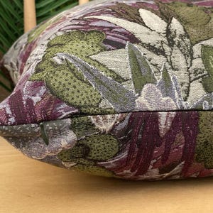 May include: A close-up of a decorative pillow with a floral pattern. The pillow is made of a textured fabric with a variety of colors, including green, purple, and white.