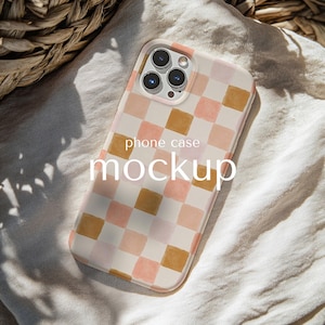 以下が含まれることがあります： ピンクとゴールドの色合いの水彩市松模様の携帯電話ケースのモックアップ。 「phone case mockup」の文字がケースに印刷されています。 ケースには白い縁とカメラの切り抜きがあります。