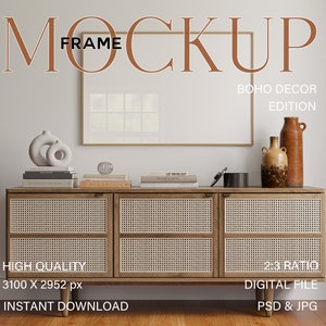 Può includere: Un mockup di una stampa incorniciata con sfondo bianco e cornice dorata, appoggiata su un mobile in legno con ante in rattan. Il mobile è decorato con due vasi in ceramica e una pila di libri. Il testo "BOHO DECOR EDITION" è visualizzato sopra la cornice.