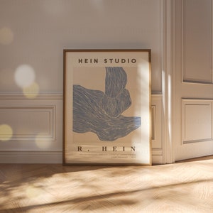 May include: A framed poster with a blue abstract design and the text "HEIN STUDIO" and "R. HEIN" in a brown frame. The poster has the text "THE LINE COLLECTION - LEISURE CITY - PRINTED BY OLIVER PRESSES - COPENHAGEN - 2017".
