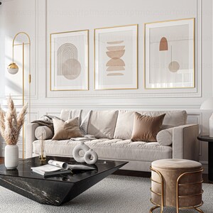 May include: A living room interior with a white couch, a black coffee table, a gold floor lamp, and three framed abstract art prints with geometric shapes in shades of brown and beige.