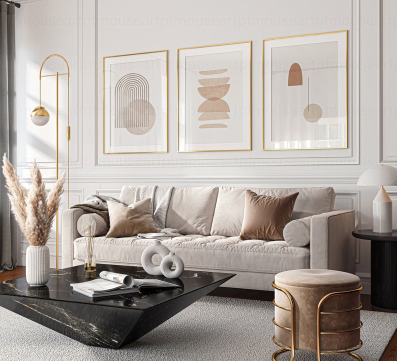 May include: A living room interior with a white couch, a black coffee table, a gold floor lamp, and three framed abstract art prints with geometric shapes in shades of brown and beige.