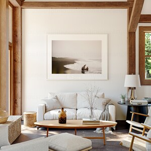 May include: A living room interior with a white sofa, a wooden coffee table, and a framed photograph of a beach scene. The room has a vaulted ceiling with exposed wooden beams.