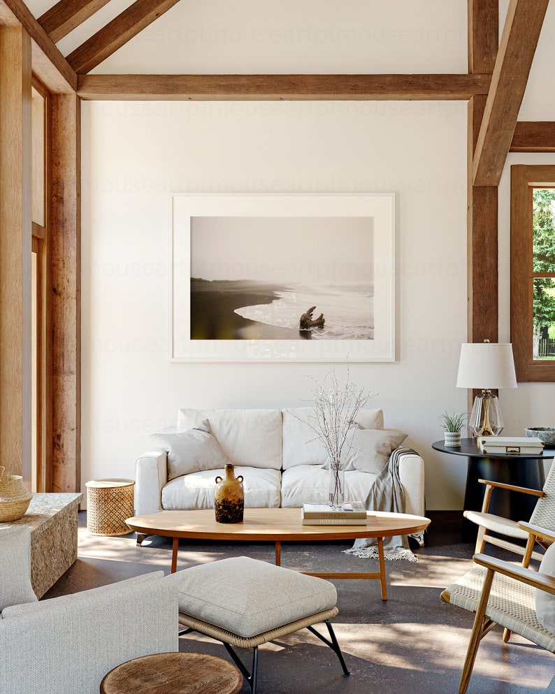 May include: A living room interior with a white sofa, a wooden coffee table, and a framed photograph of a beach scene. The room has a vaulted ceiling with exposed wooden beams.