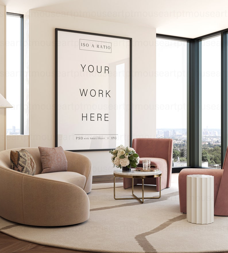 May include: A modern living room interior with a large framed poster that says "ISO A RATIO YOUR WORK HERE PSD with Smart Object + JPG". The poster is hanging on a white wall. There is a beige curved sofa with two pillows, a pink armchair, a white side table, and a coffee table with a vase of white flowers. The room has large windows with a view of a city skyline.