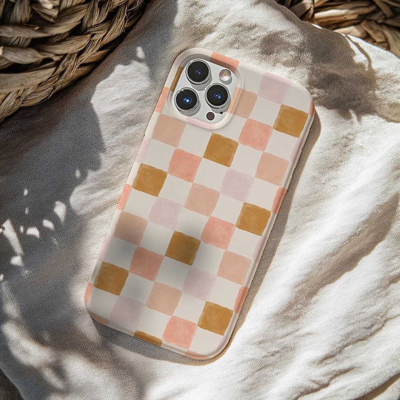 May include: A phone case with a watercolor checkerboard pattern in shades of peach, pink, and gold. The case is on a white background and has a camera lens cutout.