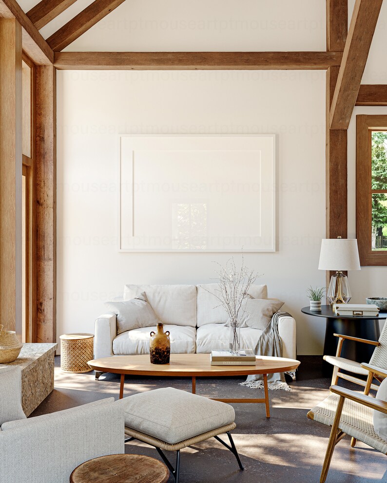 May include: A white sofa with throw pillows and a blanket sits in a living room with a wooden coffee table, a large white framed picture on the wall, and a wooden floor.
