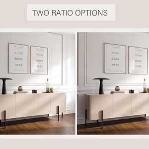 May include: Two framed prints with the text "YOUR WORK HERE" hanging on a white wall above a light beige cabinet with black legs. The cabinet is sitting on a wood floor. There is a black lamp on the left side of the cabinet and a bottle of wine on the right side of the cabinet.