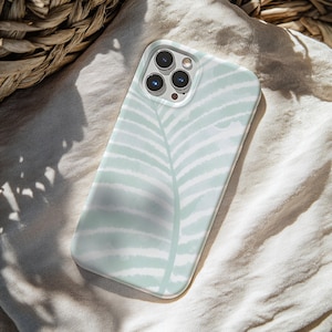 May include: A mint green and white phone case featuring a watercolor-style fern leaf design. The case has a glossy finish and is designed to fit a smartphone. The case is shown on a neutral-colored fabric.