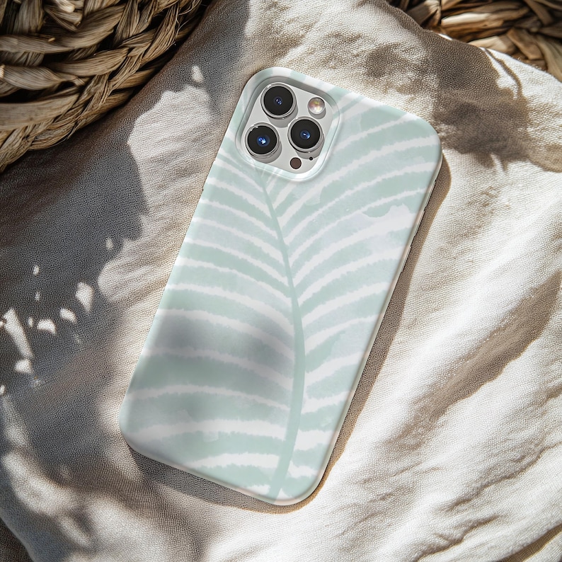 May include: A mint green and white phone case featuring a watercolor-style fern leaf design. The case has a glossy finish and is designed to fit a smartphone. The case is shown on a neutral-colored fabric.