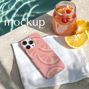 Könnte beinhalten: Rosa Handyhülle mit einem Grapefruit-Scheiben-Muster, auf einem weißen Handtuch. Ein Glas mit rosa Getränk mit Früchten und Orangenscheiben befindet sich in der Nähe. Der Text "phone case mockup" ist im Hintergrund zu sehen.