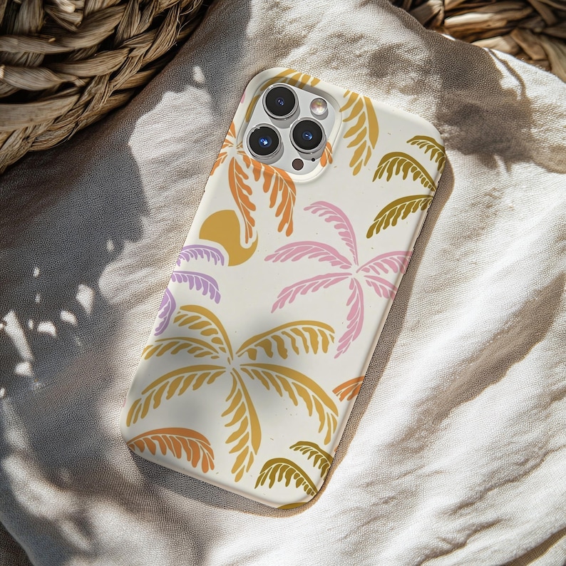 May include: A white phone case featuring a colorful tropical design. The case has a pattern of palm trees in shades of orange, pink, yellow, and green. A yellow sun shape is also included in the design. The phone case is on a white cloth.