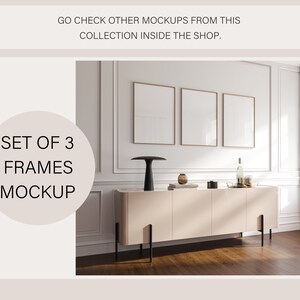 May include: A set of three empty picture frames with a light wood finish, hanging on a white wall above a light pink cabinet with black legs. The cabinet is sitting on a wood floor. The frames are all the same size and are arranged in a row.