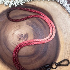 Peut inclure: Un cordon de perles en ombré rouge et noir avec un fermoir en métal noir. Le cordon est fait de petites perles et mesure environ 76 cm de long.