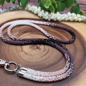 May include: A beaded lanyard with a gradient of white, pink and black beads. The lanyard has a silver swivel clasp.