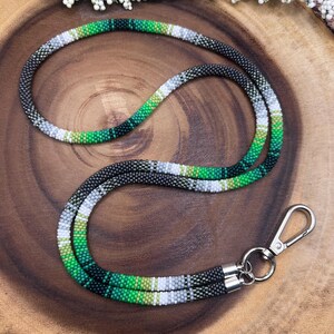 Peut inclure: Un cordon en perles vert, noir et blanc avec un fermoir pivotant argenté. Le cordon est composé de petites perles rondes et présente un motif dégradé.