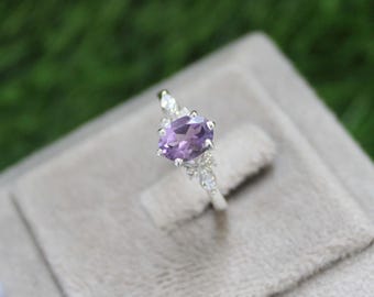 May include: A silver ring with a purple oval amethyst gemstone surrounded by smaller clear gemstones.