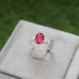 May include: A silver ring with a large oval-shaped red gemstone surrounded by smaller clear gemstones.