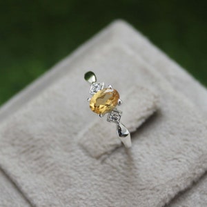 Op de afbeelding: Een zilveren ring met een gele ovale edelsteen en kleinere heldere edelstenen op de band.