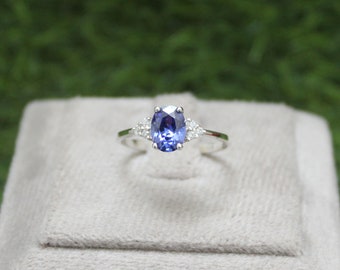 Puede incluir: Un anillo de plata con una gran piedra preciosa azul de forma ovalada rodeada de tres piedras blancas más pequeñas.