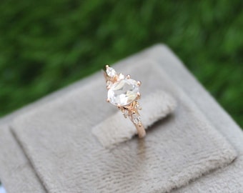 May include: A rose gold ring with a large oval-shaped clear gemstone surrounded by smaller clear gemstones.