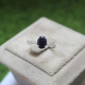 Peut inclure: Une bague en argent avec une pierre ovale bleu foncé entourée de petites pierres claires.