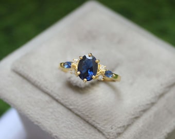 Puede incluir: Un anillo de oro con una gran piedra de zafiro azul ovalada rodeada de piedras azules y blancas más pequeñas.