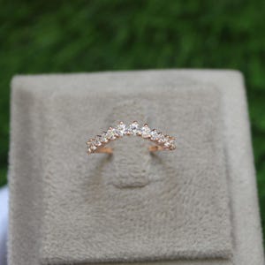 Puede incluir: Un delicado anillo de banda de oro con una fila curva de pequeños diamantes transparentes.