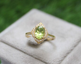 May include: A gold ring featuring a light green oval gemstone, surrounded by small white gemstones. The ring's setting has a decorative, floral-inspired design. The ring is set on a gray surface with a green background.