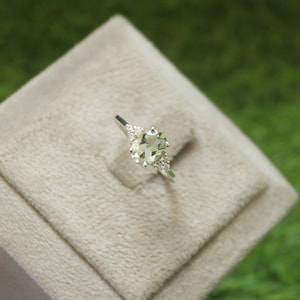 May include: A silver ring featuring a light green oval gemstone and smaller clear gemstones on the band.