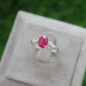 Op de afbeelding: Een zilveren ring met een grote ovale robijn, omringd door kleinere witte edelstenen.
