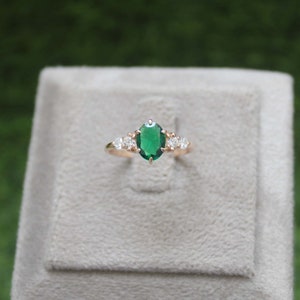 Puede incluir: Un anillo de oro con una gran piedra preciosa ovalada verde rodeada de pequeñas piedras blancas redondas.