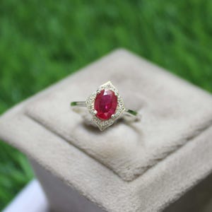 May include: A silver ring with a large oval ruby gemstone surrounded by smaller white gemstones.